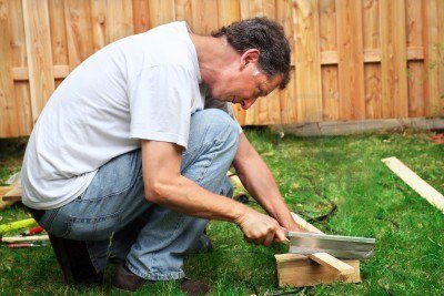 5274560-l-39-homme-accroupi--scier-un-morceau-de-bois-devant-une-cl-ture-en-bois-dans-le-jardin.jpg